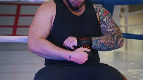 A muscular man applying elastic bandage on his wrist sitting in the gym — Stock Video