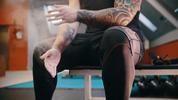 Um homem tatuado muscular cobrindo suas mãos em talco e batendo palmas a poeira se espalhando no ar — Vídeo de Stock