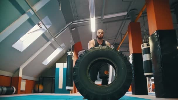 Ένας άντρας bodybuilder γυρίζοντας το λάστιχο στο πάτωμα και μετακινώντας το με αυτή την κίνηση — Αρχείο Βίντεο