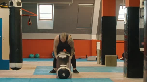 Bir adam vücut geliştirmeci yerden kum torbası çeker — Stok video