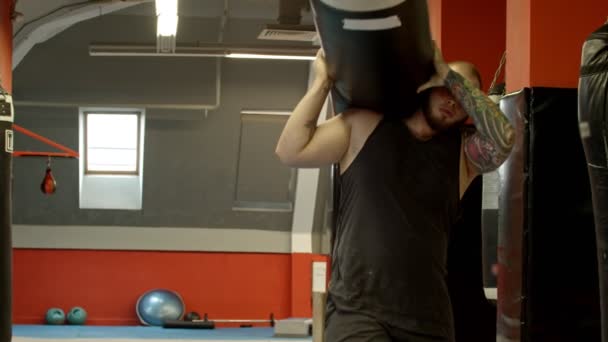 Un culturista hombre llevando el saco de boxeo en el hombro y lo pone abajo — Vídeos de Stock