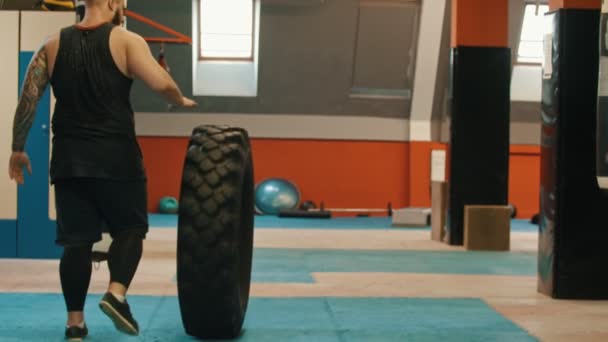 En man bodybuilder rullar ett stort däck i gymmet — Stockvideo