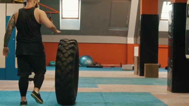 Ein Mann Bodybuilder rollt einen großen Reifen in der Turnhalle — Stockvideo