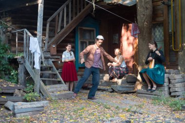 Sakallı bir adam rus halk dansları dans - kadın kır evinin yakınındaki merdivenlerde oturan ve onu izlerken ve el çırparak - balalaika oynayan bir kadın