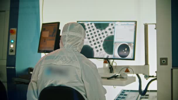 Un trabajador con traje protector blanco y protector sentado junto al monitor - laboratorio de investigación del cosmos — Vídeo de stock