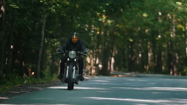 Een brute man motorrijder in helm rijden een motorfiets in het bos — Stockvideo
