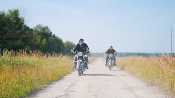 Két férfi motorosok lovaglás motorbiciklit a rozs területen-poros út — Stock videók