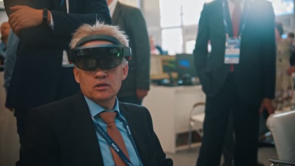 29. srpen 2019 Moskva, Rusko: výstava technologií-starý obchodník sedící ve VR a hovořícího se svými kolegy — Stock video