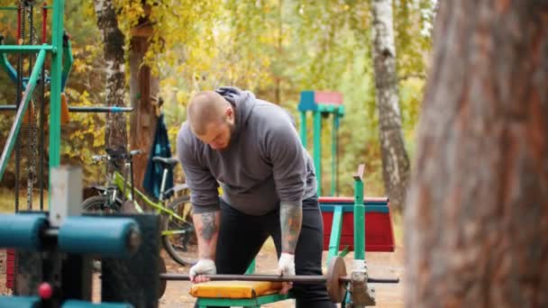 Een man bodybuilder trekt de zelfgemaakte dumbbells-training op het buiten sportterrein — Stockvideo