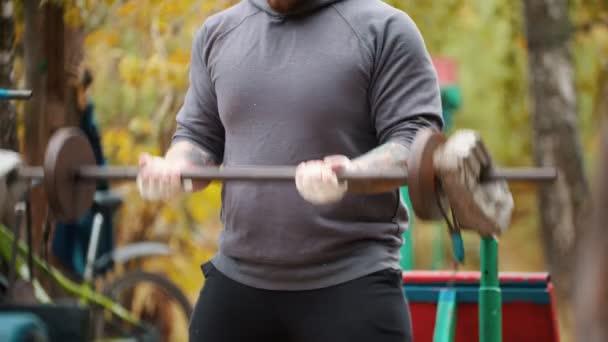 Ένας άντρας bodybuilder που αντλεί τα χέρια του με τα βαράκια κατασκευασμένα από τούβλα και βάρη-εκπαίδευση στο ύπαιθρο αθλητικό έδαφος — Αρχείο Βίντεο