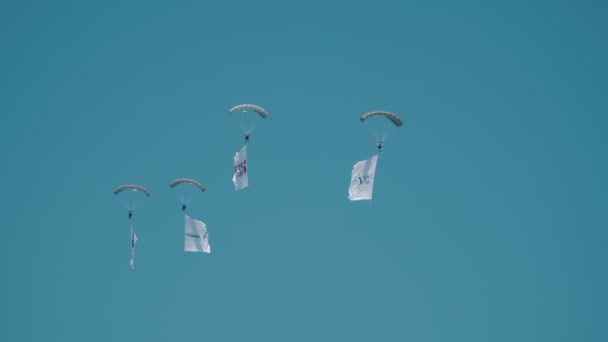 30 augustus 2019 Moskou, Rusland: vier mannen vliegen in de lucht met geopende parachute houden vlaggen met logo van Vliegtuigproductie bedrijven — Stockvideo