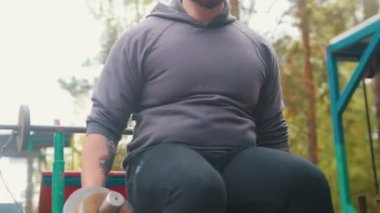 Bir dövmeli adam vücut geliştirmeci halter çeker - açık hava çocuk spor zemin eğitim