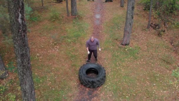 Ein tätowierter harter Mann Bodybuilder schiebt über den Reifen auf dem Boden im Wald — Stockvideo