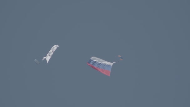 30 AGOSTO 2019 MOSCÚ, RUSIA: Dos personas ondeando en el cielo nublado con paracaídas abiertos sosteniendo la bandera con el logotipo de la compañía de fabricación de aviones y la bandera nacional rusa — Vídeos de Stock