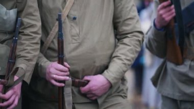 Several soldiers in warm coats standing in the row holding guns - one of them holding a cigarette