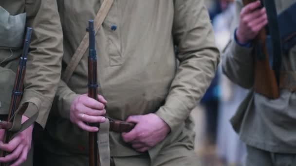 Несколько солдат в теплых пальто стоят в ряду, держа в руках оружие - один из них держит сигарету — стоковое видео