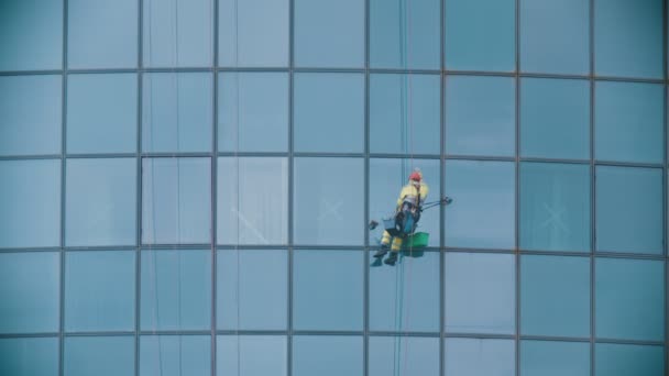 Человек-рабочий висит на веревках у наружных окон небоскреба и чистит их - индустриальный альпинизм — стоковое видео