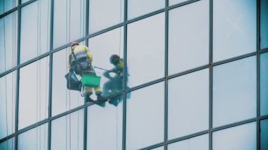 İplere asılmış bir işçi bir iş gökdeleninin dış camlarını siliyor. Endüstriyel dağcılık.