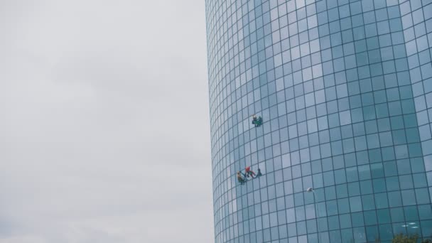 Drei Männer Arbeiter hängen an Seilen an den äußeren blauen Fenstern eines Wolkenkratzers - industrieller Alpinismus - Herbstzeit und bewölktes Wetter — Stockvideo