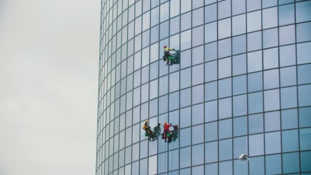 Three men workers hanging on ropes and cleaning the exterior glass windows of a business skyscraper after rain - autumn time and overcast weather — Stock Video