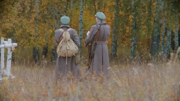 Twee volwassen soldaten in warme jassen die op het veld voor het herfstbos staan en met elkaar praten — Stockvideo