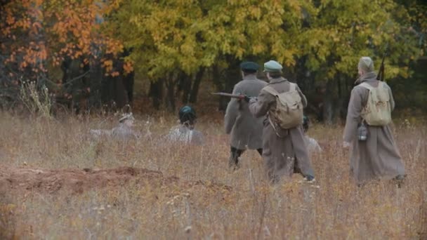 Varios soldados en abrigos calientes caminando en el campo frente al bosque de otoño - otro soldado sentado en el suelo — Vídeo de stock