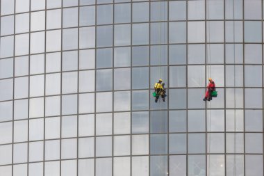 İki erkek işçi bir gökdelenin dış camlarında ipe asılıyor ve onları temizliyor - endüstriyel dağcılık - sonbahar zamanı ve bulutlu hava