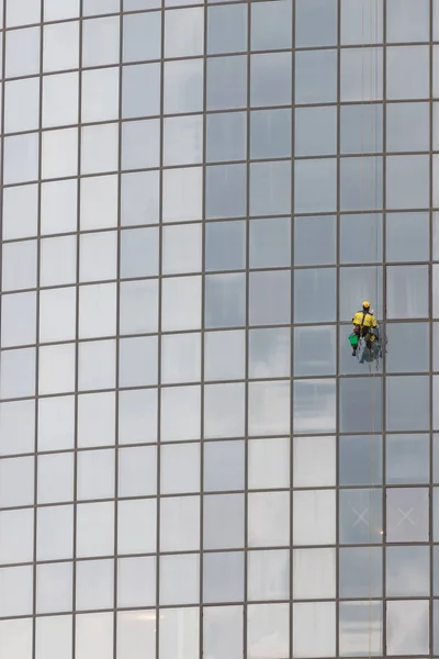 Ein Arbeiter im Arbeitsanzug reinigt die Außenfenster eines Wolkenkratzers - industrieller Alpinismus - hängt an Seilen — Stockfoto