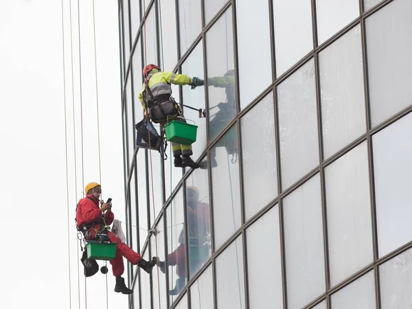 İki işçi bir gökdelenin dış camlarında asılı halatlarla onları temizliyor - endüstriyel dağcılık - bulutlu hava
