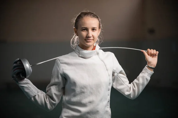 Een jonge glimlachende vrouwelijke schermer die in de sportschool staat met een zwaard achter haar rug — Stockfoto