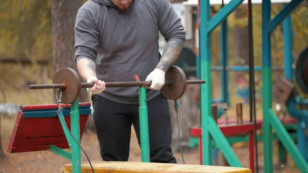 En man bodybuilder drar upp den egentillverkade hantlar-utbildning på utomhus idrottsplats — Stockfoto
