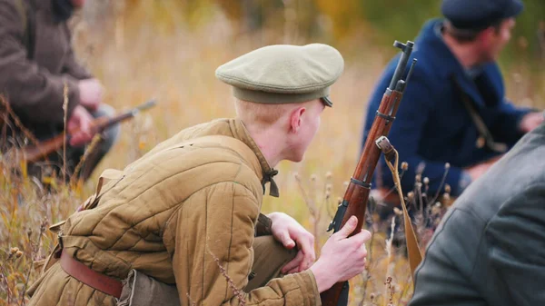 Wojskowy człowiek siedzi na boisku z bronią z innymi żołnierzami. — Zdjęcie stockowe