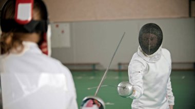 Eskrimciler spor salonunda birbirlerine saldırıyorlar.