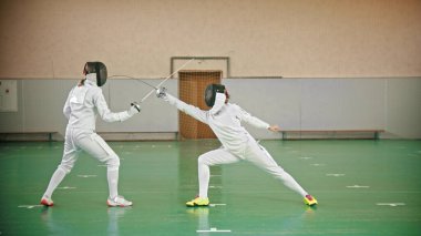 Okulun spor salonunda iki eskrimci kavga ediyor.