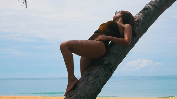Молодая женщина прислонилась к пальме возле океана — стоковое фото