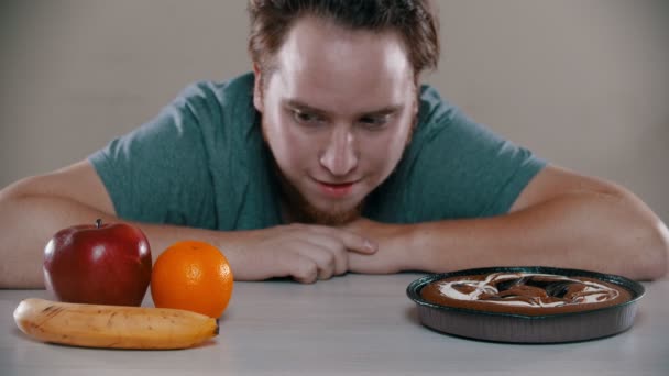 Homem está escolhendo entre bolo e frutas na mesa — Vídeo de Stock