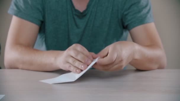 Человек складывает белый бумажный самолет на столе — стоковое видео