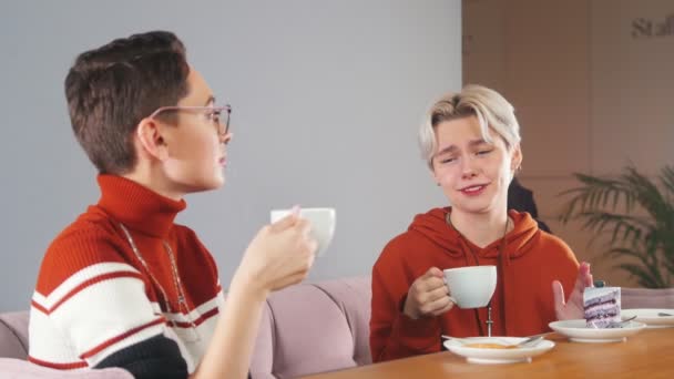 Дві молоді дівчата сидять поруч в кафе і сміються — стокове відео