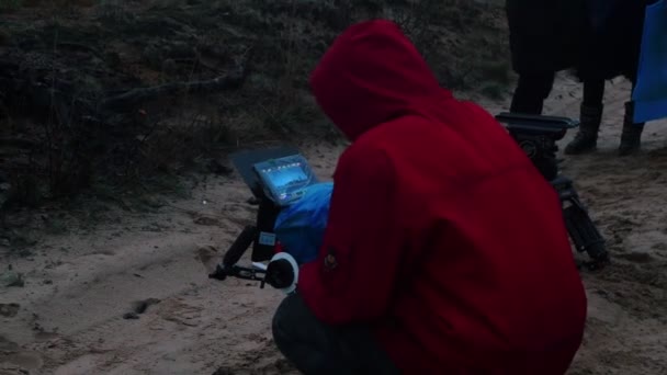 Un hombre con chaqueta roja sosteniendo una cámara y filmando una escena de cine en el bosque — Vídeo de stock