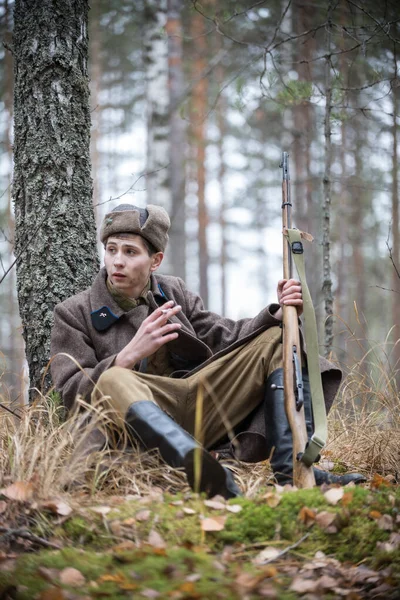 2. Dünya Savaşı 'ndan kalma tüfekli bir asker ağaçta oturmuş sigara içiyor. — Stok fotoğraf