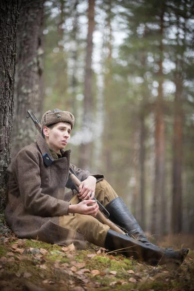 Un soldado de la Segunda Guerra Mundial vestido de militar está sentado en el bosque y fumando — Foto de Stock