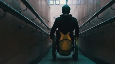 Tekerlekli sandalyedeki engelli adam metrodaki uzun rampadan iniyor.