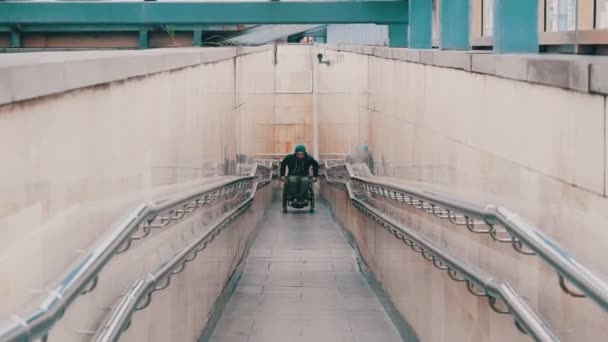 Disabled man in wheelchair getting up on the long special ramp with an effort — 비디오