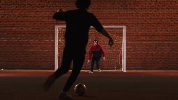 Zwei junge Männer spielen nachts Fußball auf dem Spielplatz — Stockvideo