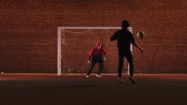 Twee jonge vrienden die 's avonds voetballen op de buitenspeelplaats — Stockvideo