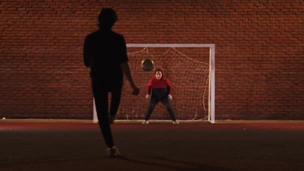 Két fiatal barát focizik a szabadtéri játszótéren éjjel - védik a kapukat — Stock videók