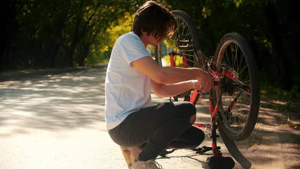 Молодой человек чинит велосипед в парке — стоковое фото
