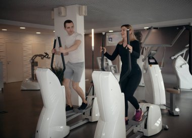 Modern spor salonu. Beyaz tişörtlü bir adam ve spor salonunda sabah egzersizi yapan bir kadın.