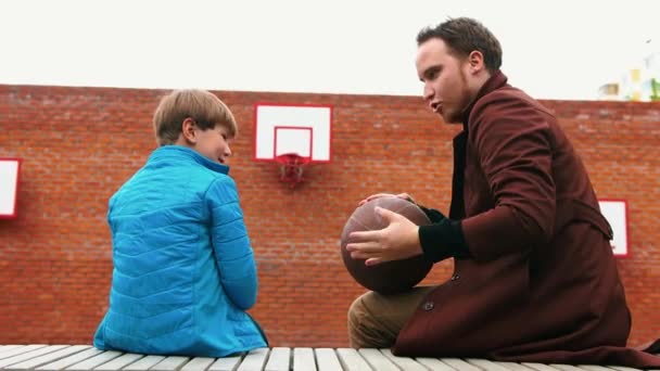 Joven y su hermano pequeño en el patio de baloncesto — Vídeo de stock