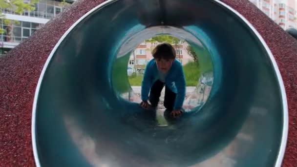 En liten pojke leker på lekplatsen - kryper genom röret — Stockvideo